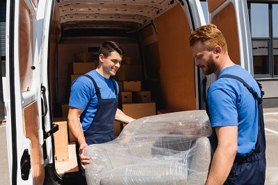 Movers carrying armchair in truck on urban street